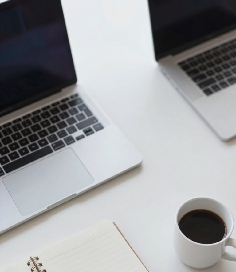 An overhead view of a clean desk with a laptop, a notebook, and a coffee cup. High contrast and professional lighting. Elements of the desk are in shades of #4E7B99 and #F5F8FA, reflecting a focused and efficient work environment.