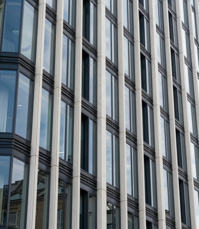 A close-up photograph of modern architectural glass and steel cladding on a sustainable building in a French / European urban district. The lighting is crisp, reflecting steel blue and off-white tones.