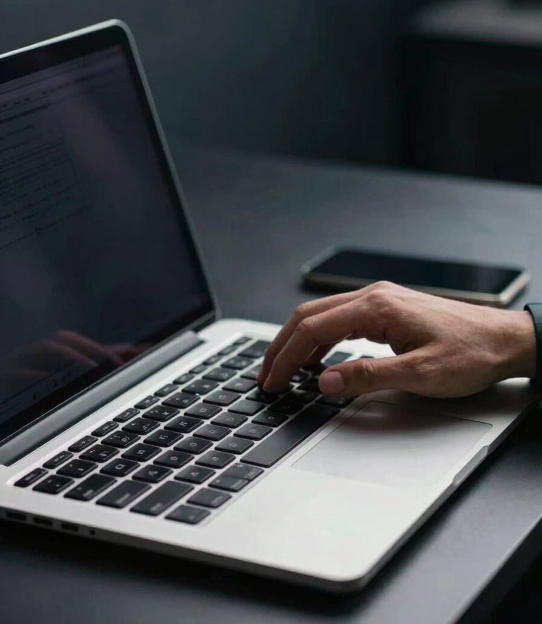 A close-up of a professional workstation with a sleek laptop. A person is typing efficiently. The setting is clean and modern with dark navy and cool grey tones in the background. Soft, empowering lighting.