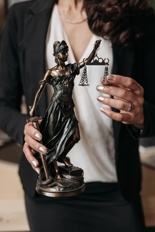 Abogada sosteniendo una estatua de la justicia con balanza, en un entorno profesional.