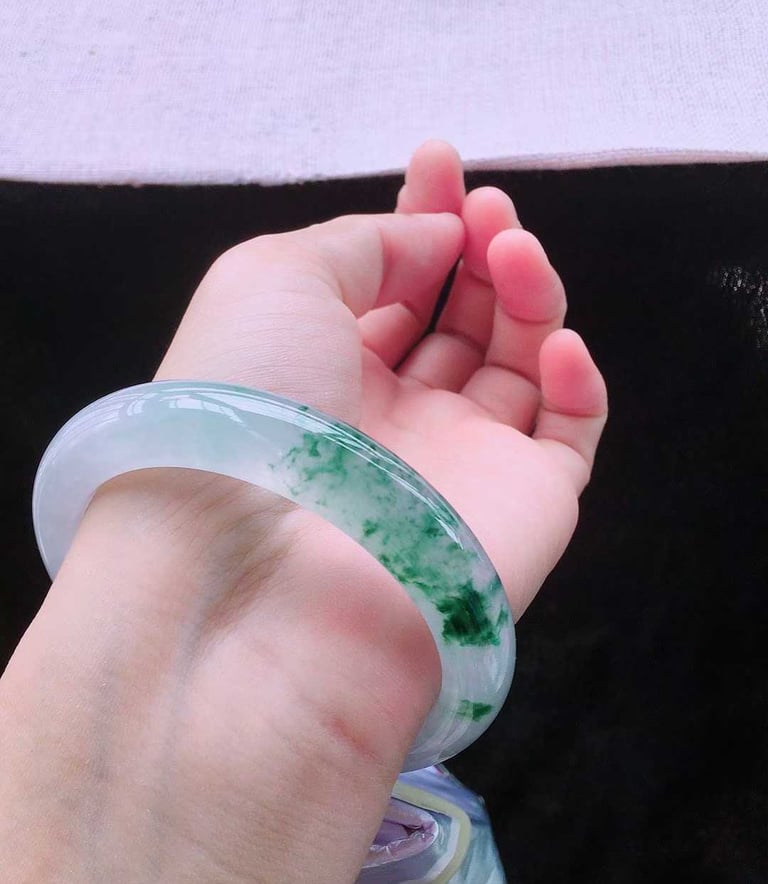 A person wearing a translucent green and white jadeite jade bangle bracelet on their wrist.