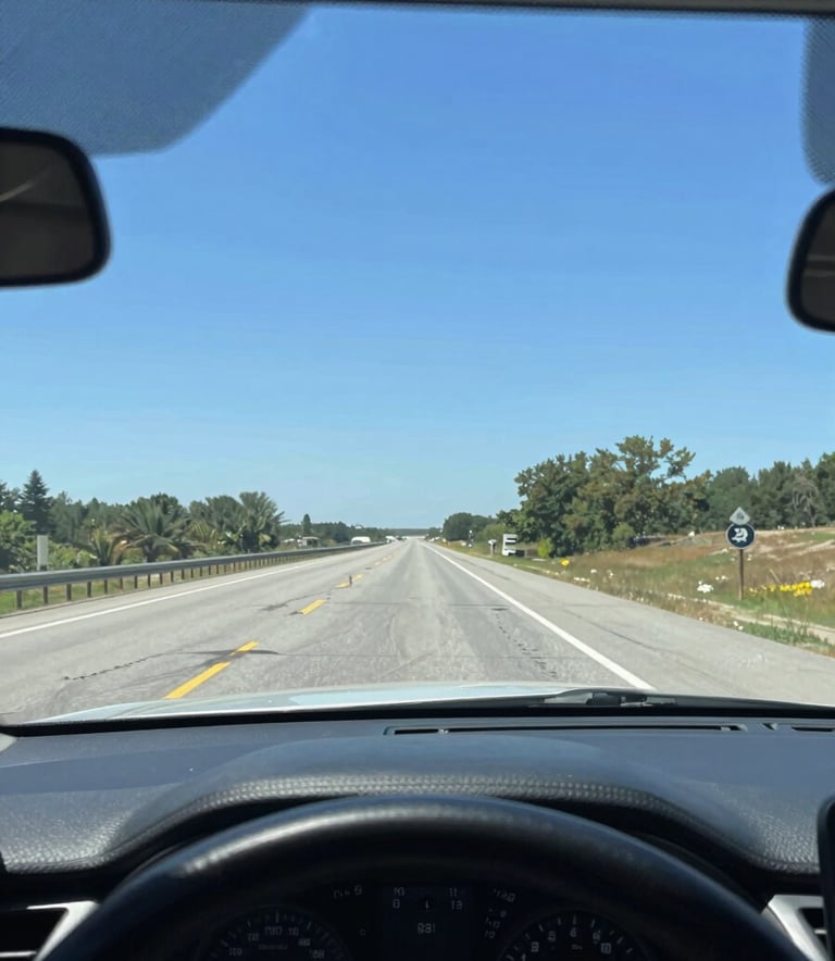A bright, high-clarity photograph looking through a perfectly clean car windshield from the interior. The view shows a scenic North American highway stretching forward under a bright blue sky. The dashboard is clean and modern, conveying a sense of safety and a clear path ahead.