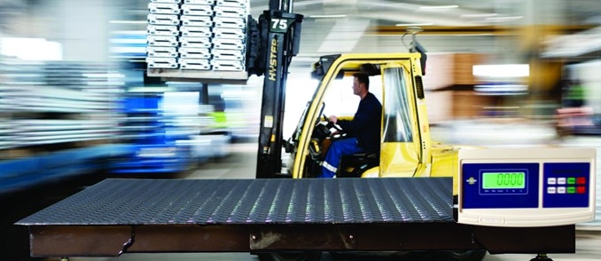 Industrial floor scale with digital display in a warehouse with a forklift moving inventory.