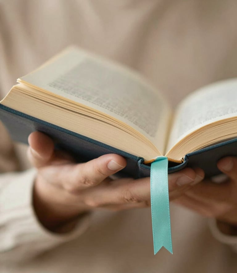 A close-up, elegant shot of a person's hands holding a book manuscript, with a soft turquoise ribbon bookmark. The lighting is warm and inspiring, suggesting a sacred work. Colors: #A1D4D0, #C7A196, #FDF7F5.