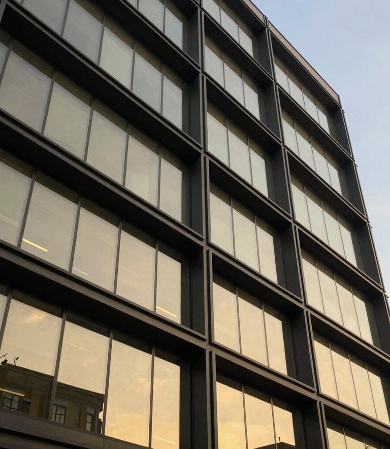 A low-angle shot of a sleek, modern South African commercial building facade with dark grey steel beams and gold-tinted architectural glass, reflecting a clear sky. Luxury minimalist style.