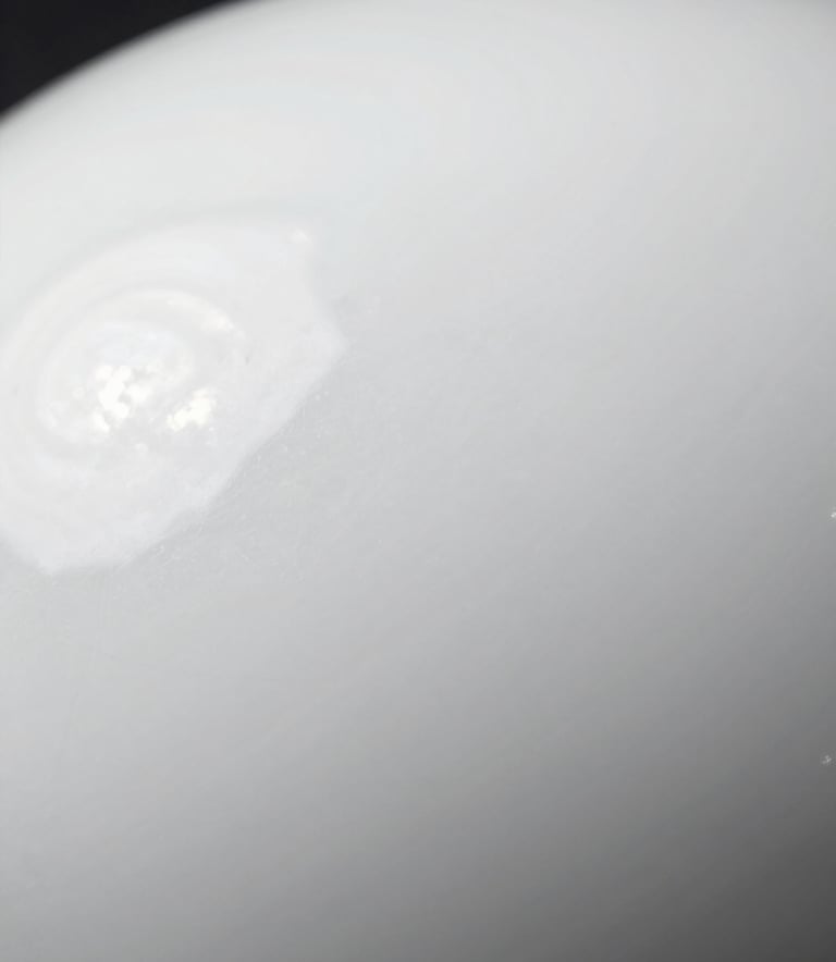 Close-up macro shot of a flawlessly smooth and glossy white ceramic surface with clean reflections, bright studio lighting, emphasizing the premium quality of the finish.