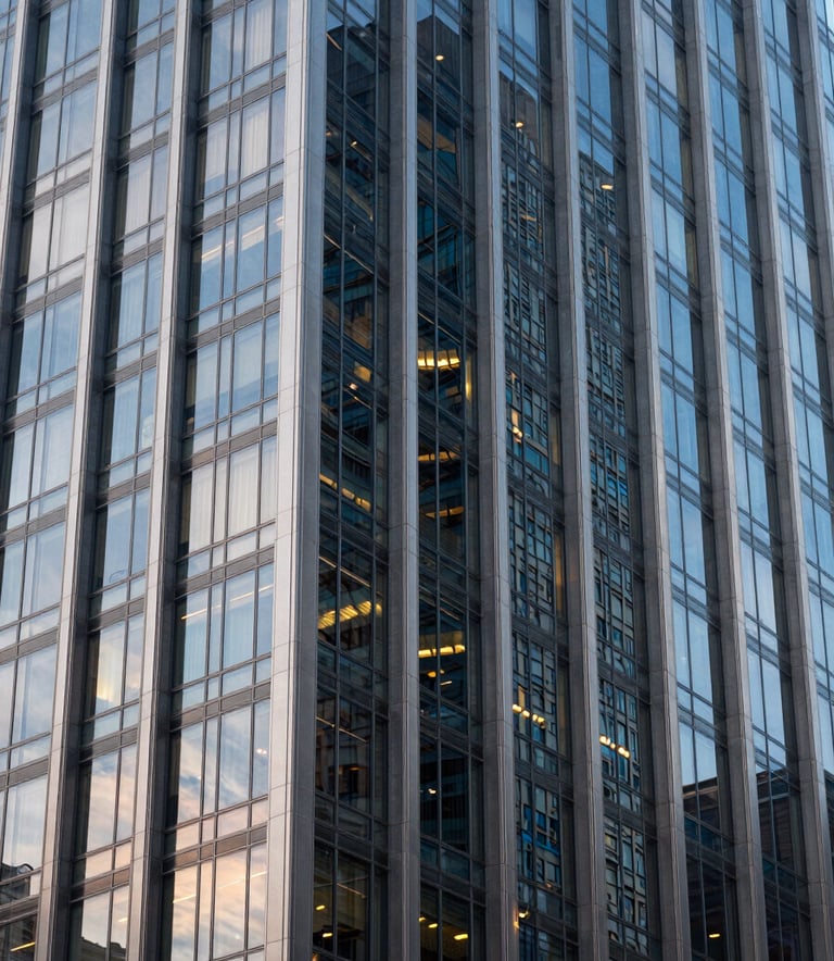 A close-up of a contemporary glass and steel skyscraper facade in a US city at dusk, showing light grey and dark blue reflections with sharp architectural focus.