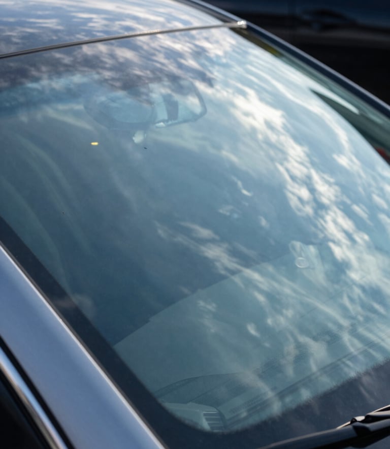 Close-up of a perfectly clean and shiny luxury car windshield reflecting a bright blue North American sky with light wispy clouds, emphasizing safety and clarity, high-end photography, sharp focus.