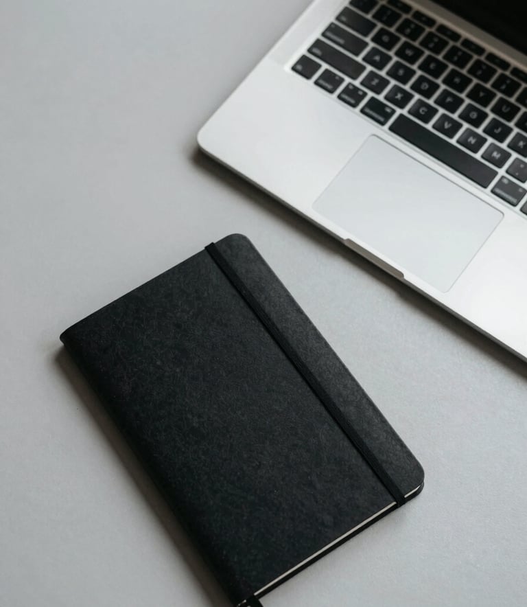 A top-down view of a minimalist desk setup with a sleek laptop and a single black notebook on a light gray surface, professional North American office setting, clean lines and clutter-free.