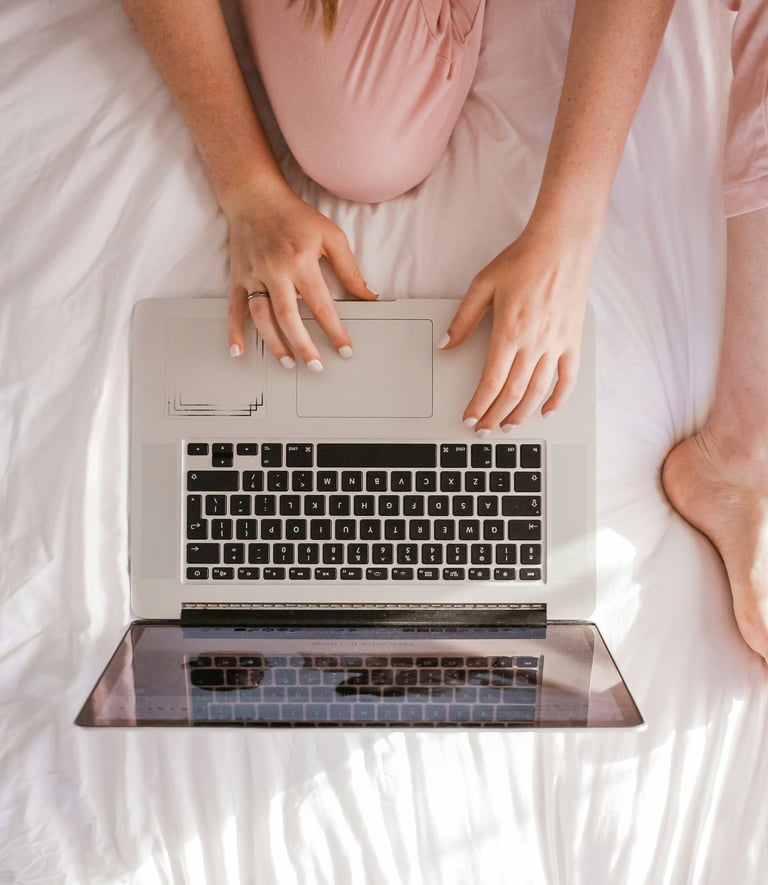 a woman sitting on a bed with her laptop computer
