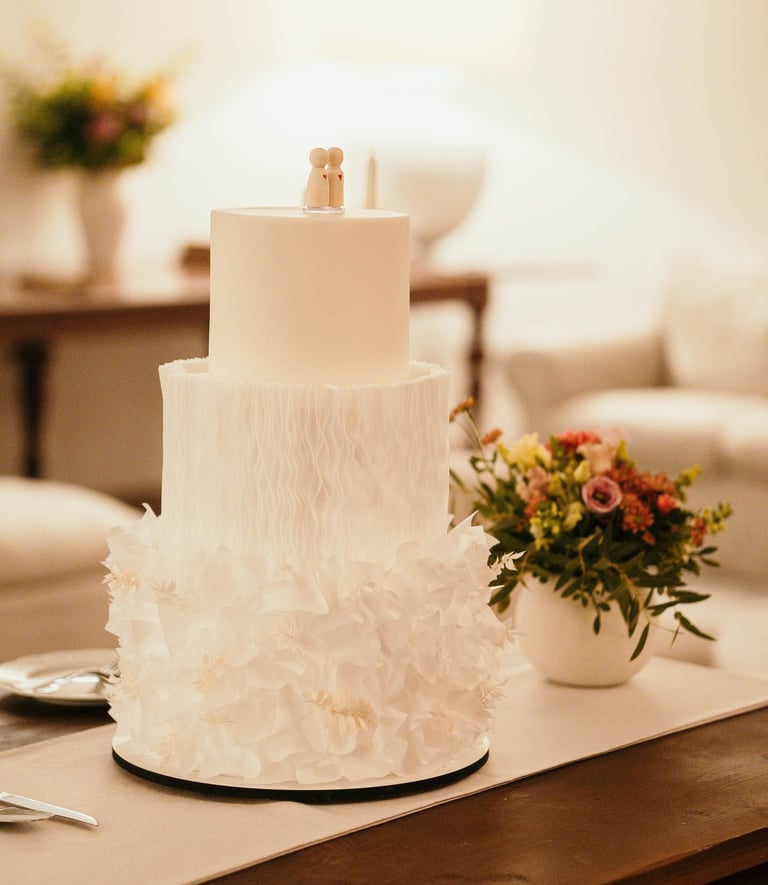 Elegant three-tier white wedding cake with textured ruffles and a minimalist peg doll topper.