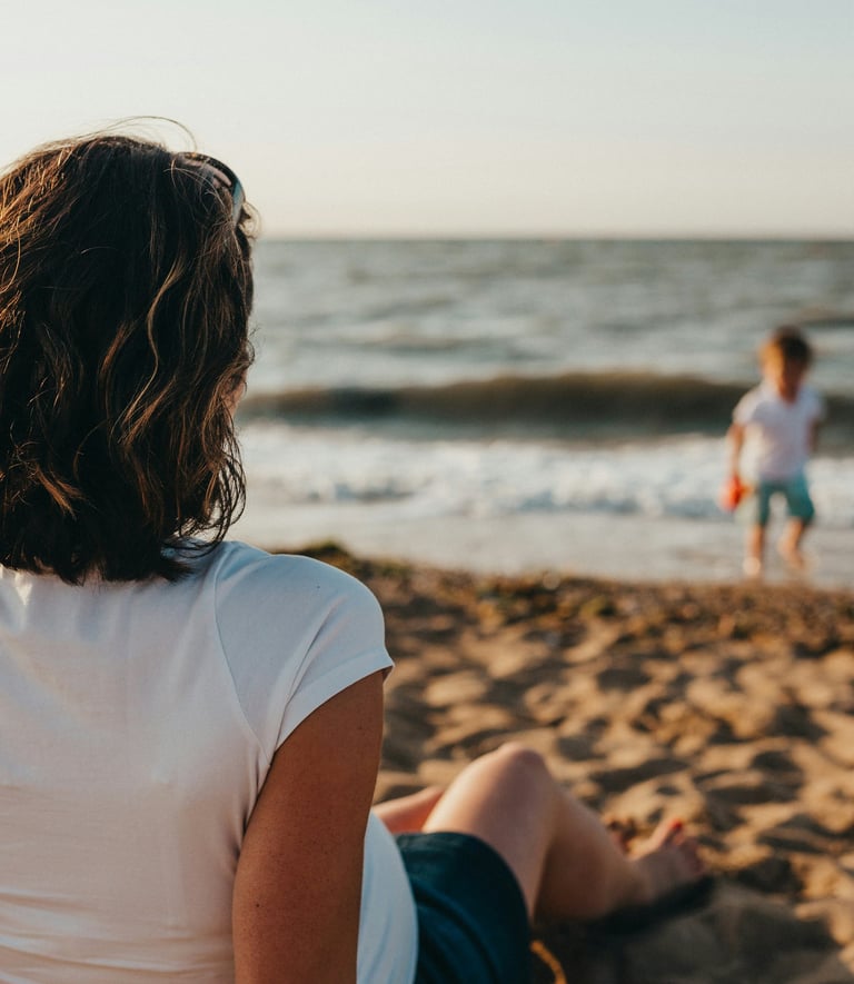 Mère assise sur la plage, face à la mer, regarde son fils jouer au bord de l'eau