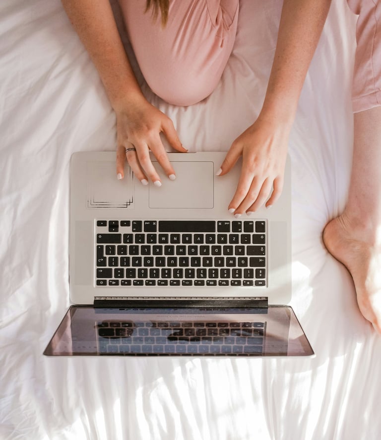 a woman sitting on a bed with her laptop computer