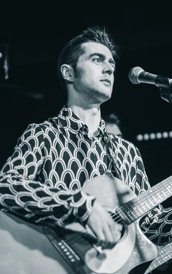 Rock and roll singer Olly Williams in Brighton, captured in black and white while performing with acoustic guitar.