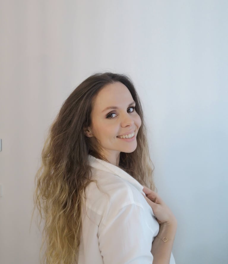 Smiling woman with long wavy brown hair wearing a white button-down shirt against a neutral background.