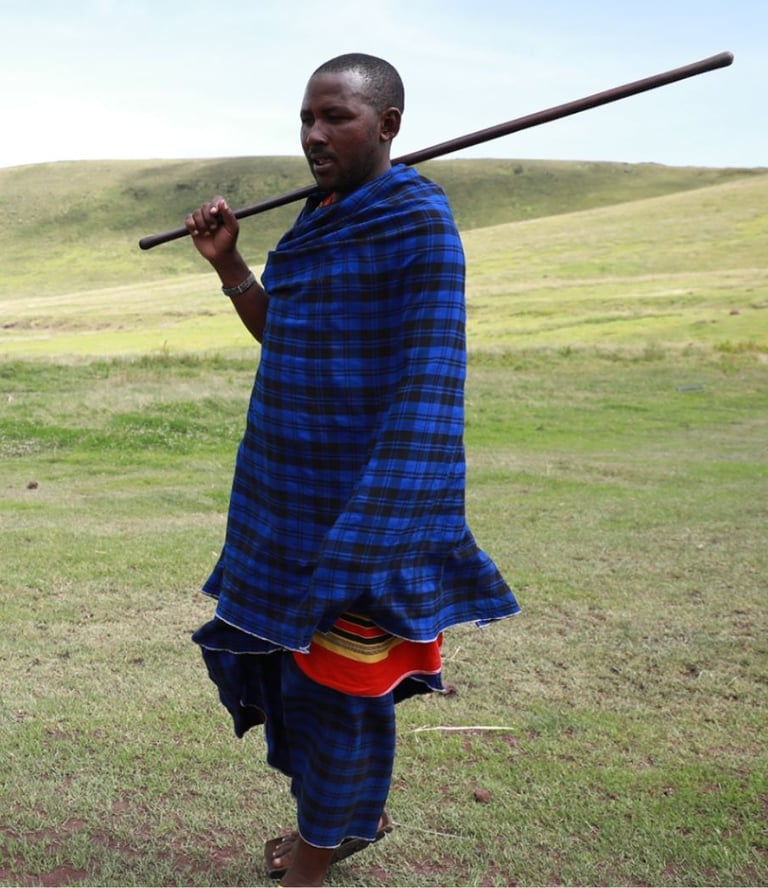 A Maasai Warrior in a blue and black outfit holding a stick in his hand