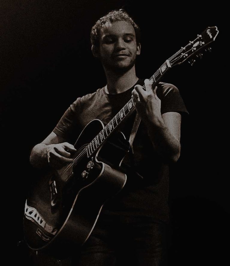 Luann Abossolo Foh live on stage with an acoustic-electric guitar in a dark concert setting.