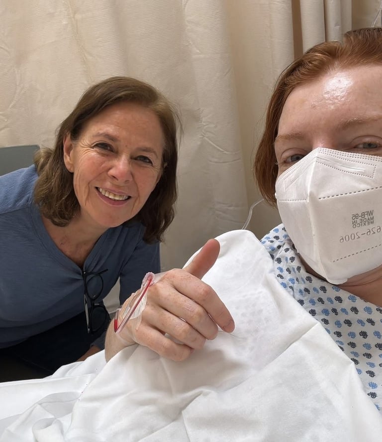 Liz sitting next to a client as she sits in a hospital bed holding a thumbs up