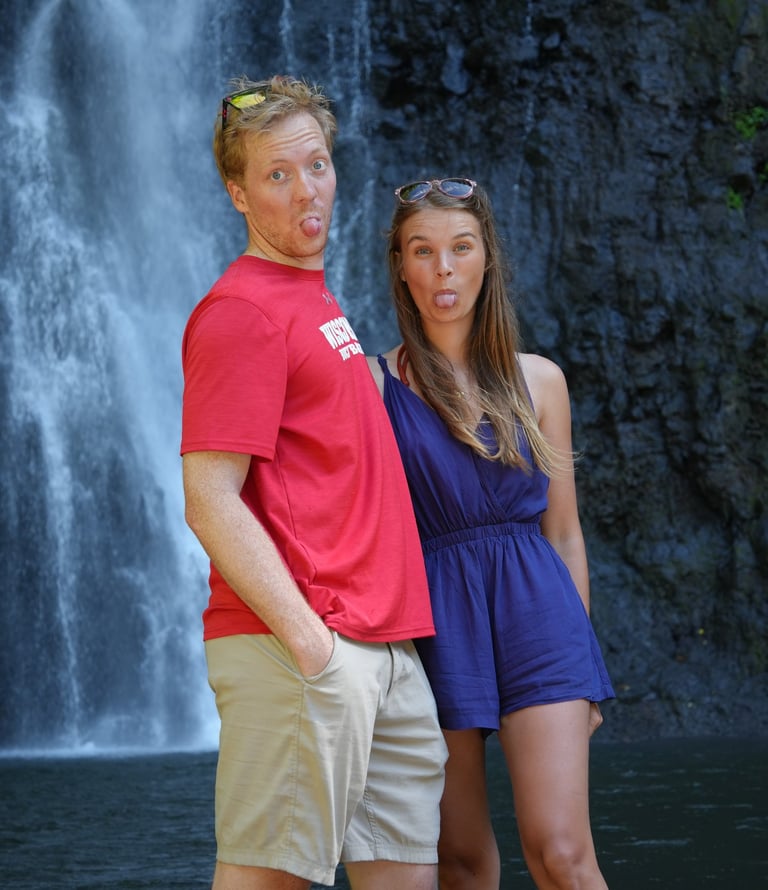 Alex and Niccy sticking out their tongues in front of a waterfall in Tahiti