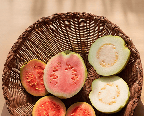 Fresh pink and white guava slices arranged in a rustic wicker basket on a sunny table.