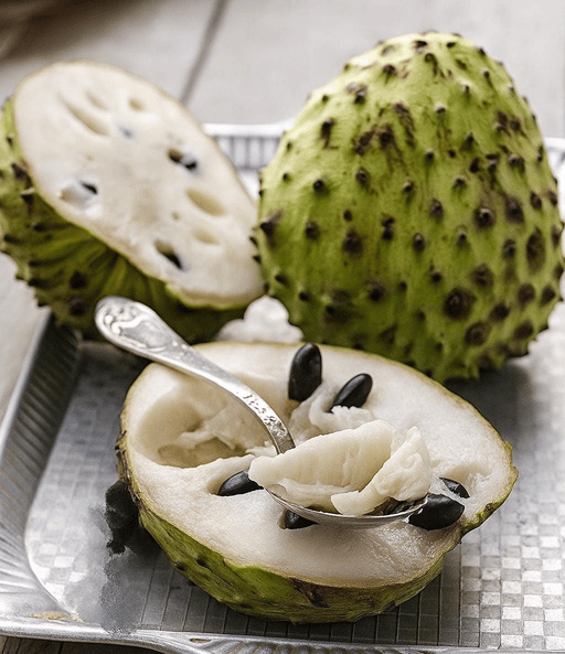 Fresh soursop fruit sliced open on a tray with white pulp and black seeds.