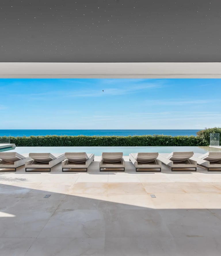 Luxury poolside patio with lounge chairs overlooking a modern infinity pool and the blue ocean.