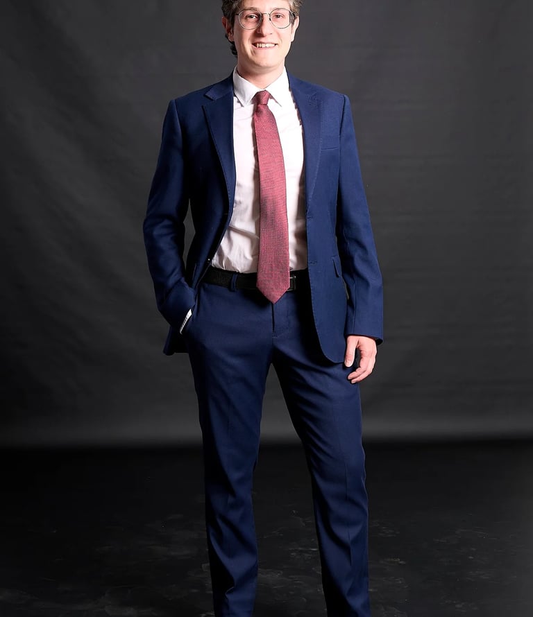 Professional man in a blue tailored suit and red tie posing for a corporate headshot.