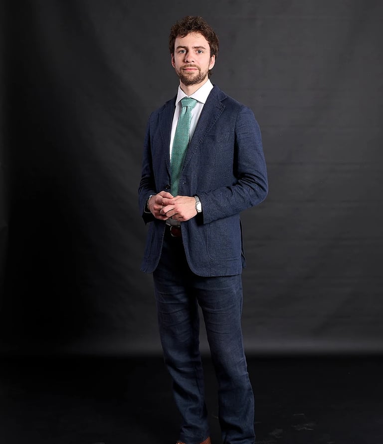 Professional man in a blue textured suit and green tie posing against a black background.