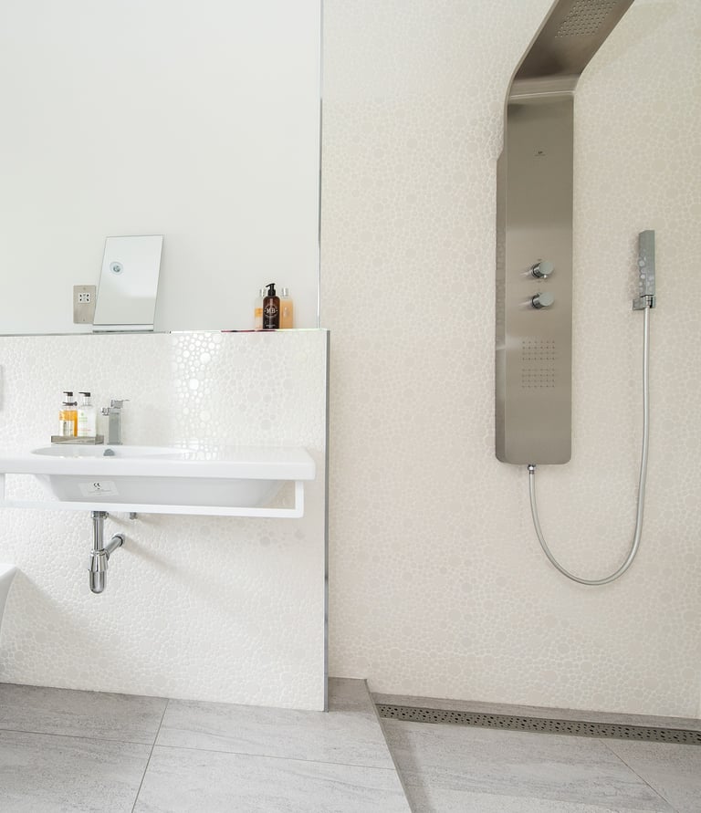 A modern, white bathroom showing a wall mounted sink and an electric shower. 