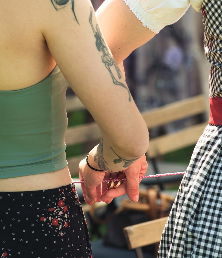 Hände halten Eheringe an einer Schnur hinter dem Rücken. Kreatives Hochzeitsdetail von Joel Pingel.