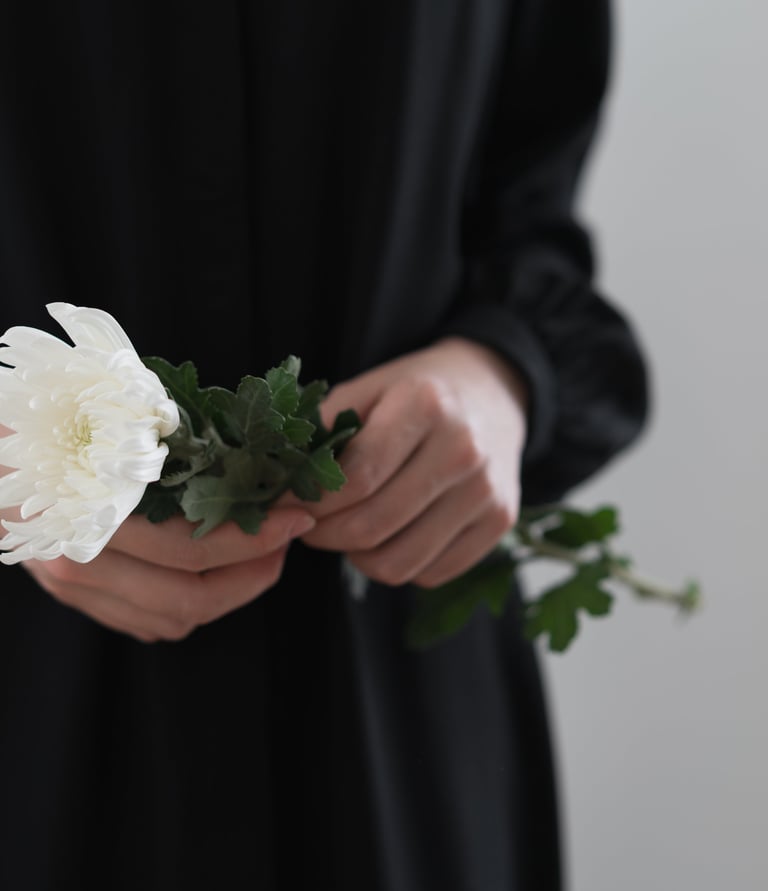 Woman gently holding a white chrysanthemum flower in remembrance.