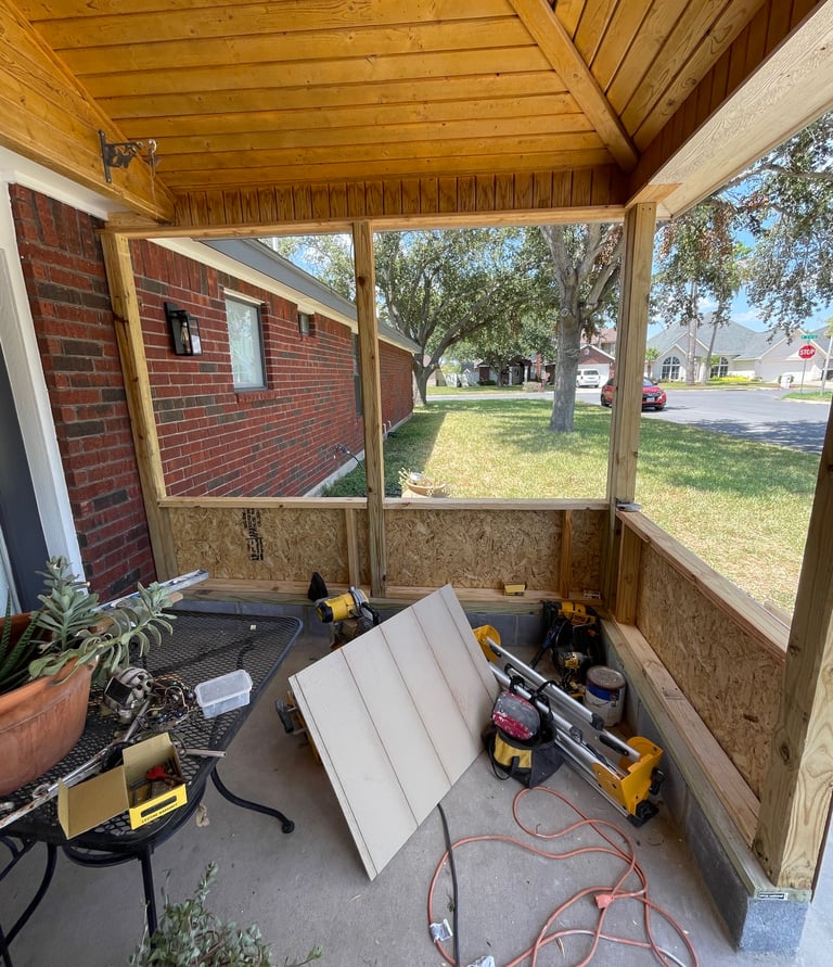 A backyard porch renovation under construction with new wood ceiling and screen enclosure framing.