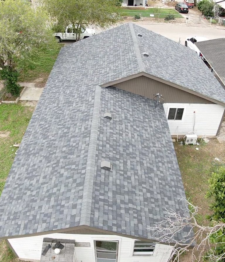 Aerial view of a residential home with newly installed grey architectural asphalt shingles on a gabled roof.