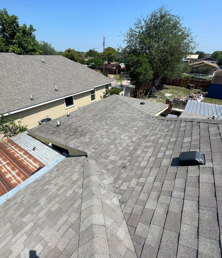 Elevated view of a residential roof featuring gray asphalt shingles and a roof vent in a suburban neighborhood.