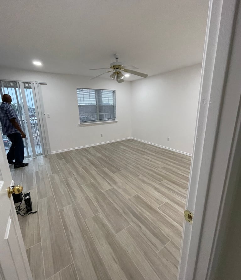 Empty modern living room featuring light wood-look tile flooring, white walls, and a ceiling fan with lights.