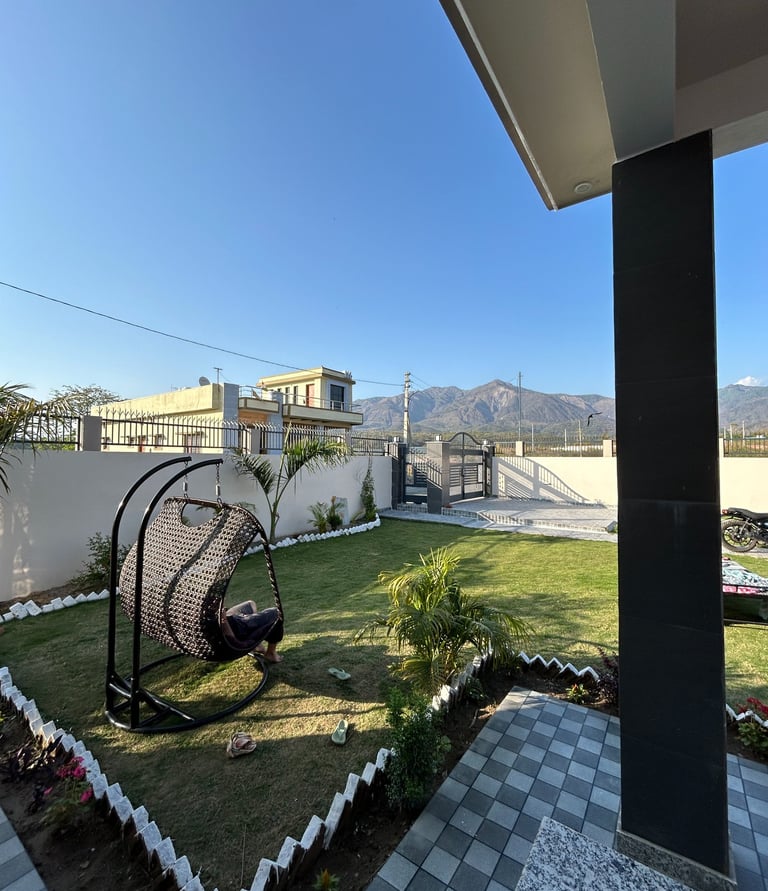 A modern garden landscape featuring a wicker hanging egg chair on a lush green lawn with mountain views.