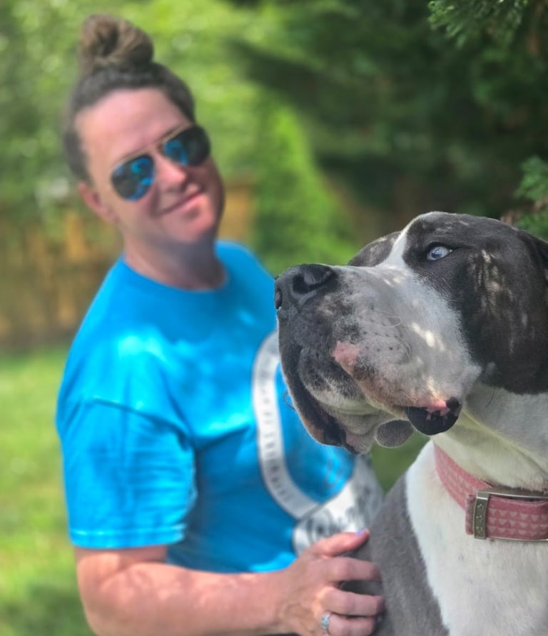 a woman in a blue shirt and sunglasses is holding a dog