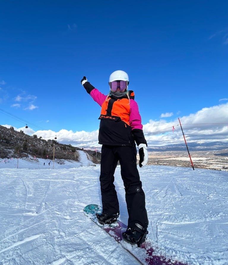 Whitney enjoying a day on the slopes while snowboarding in winter gear.