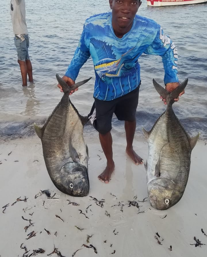 a man holding two fish on the beach