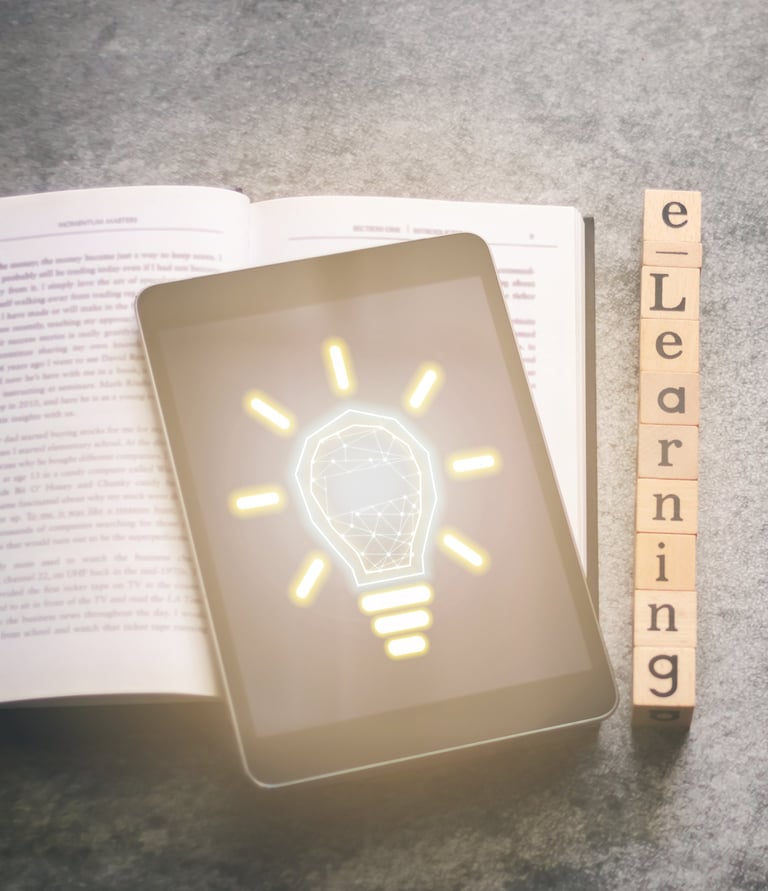 A tablet computer sits on an open book displays the image of a shining lightbulb with a brain in it.