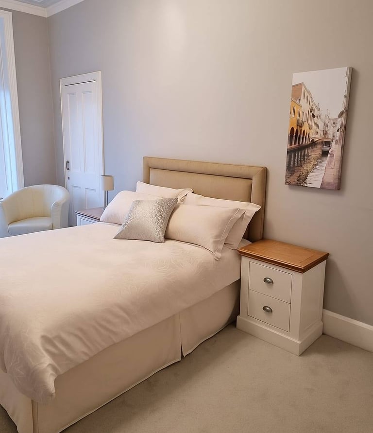 Neutral modern bedroom with a beige upholstered headboard, white nightstand, and Venice wall art.