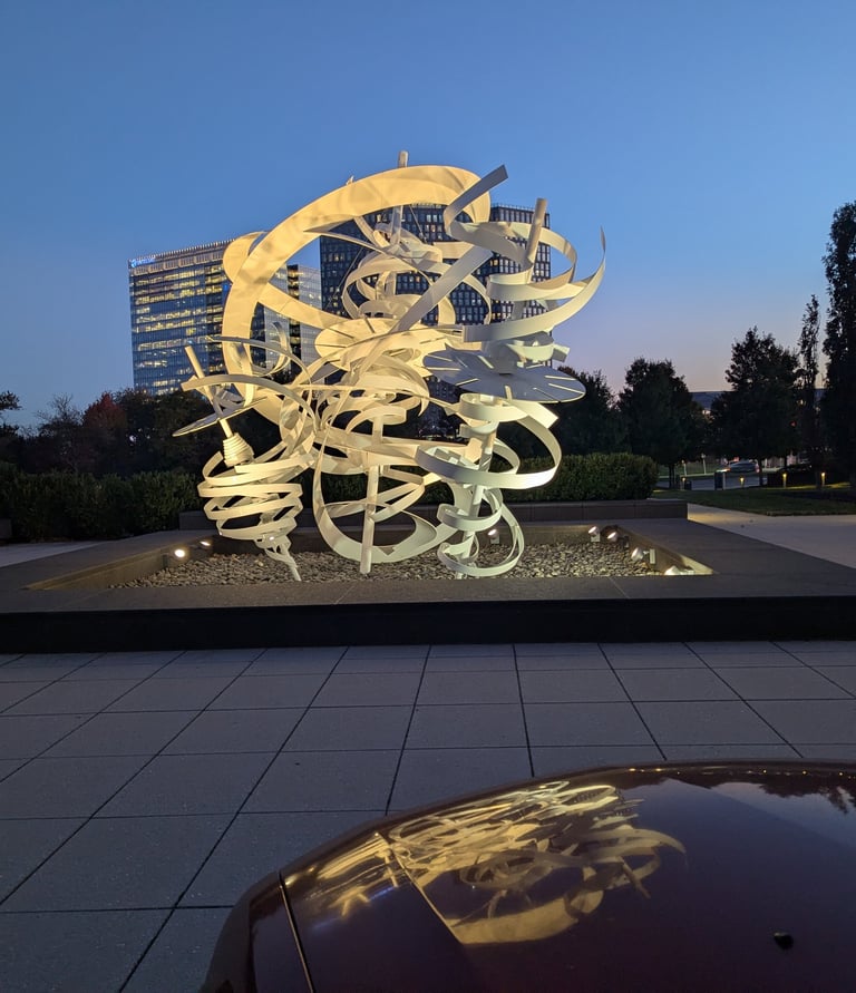 a sculpture and modern buildings during the golden hour