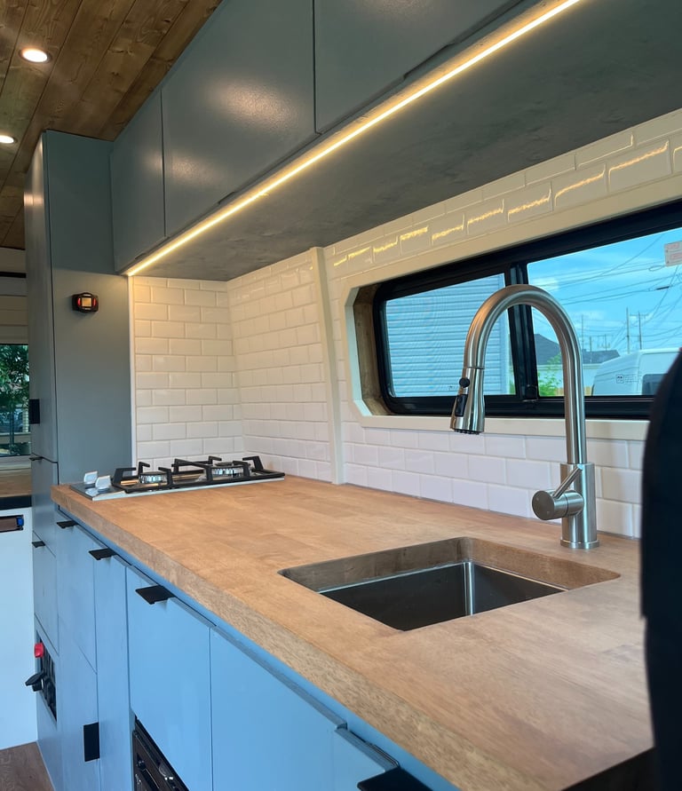 wooden countertop with beautiful backsplash inside van with sink and stovetop