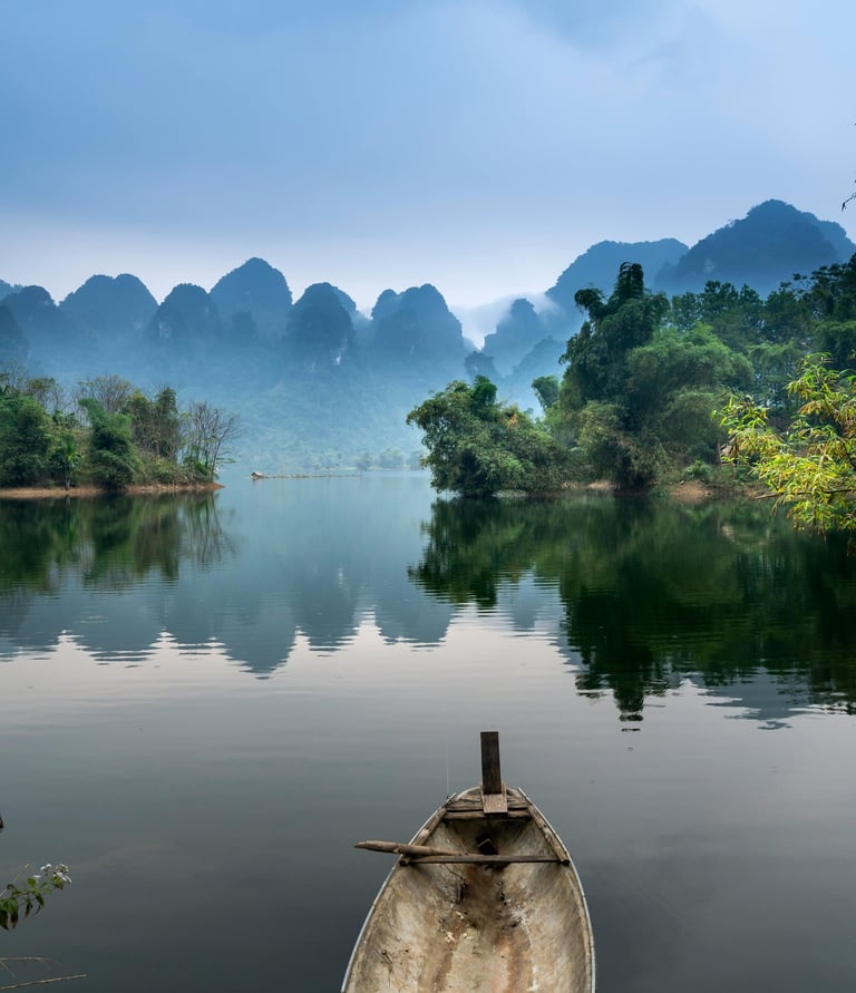 Ein asiatisches kleines Boot an einem Ufer mit schau auf einen Fluss und Hügel im Hintergrund.