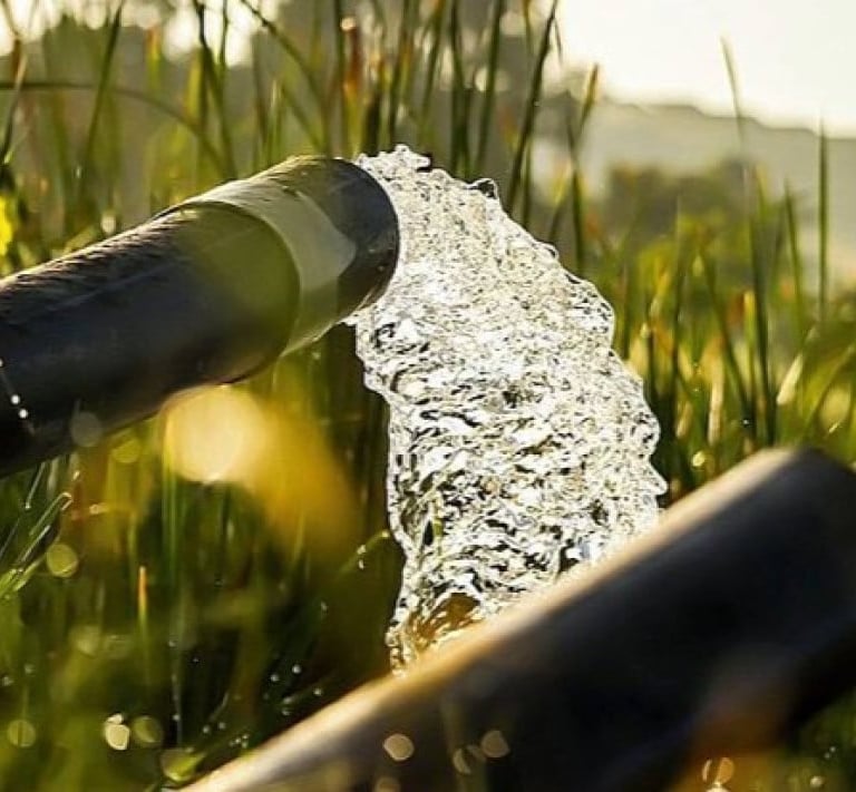 Clear water flowing from an agricultural irrigation pipe into a green field at sunrise.
