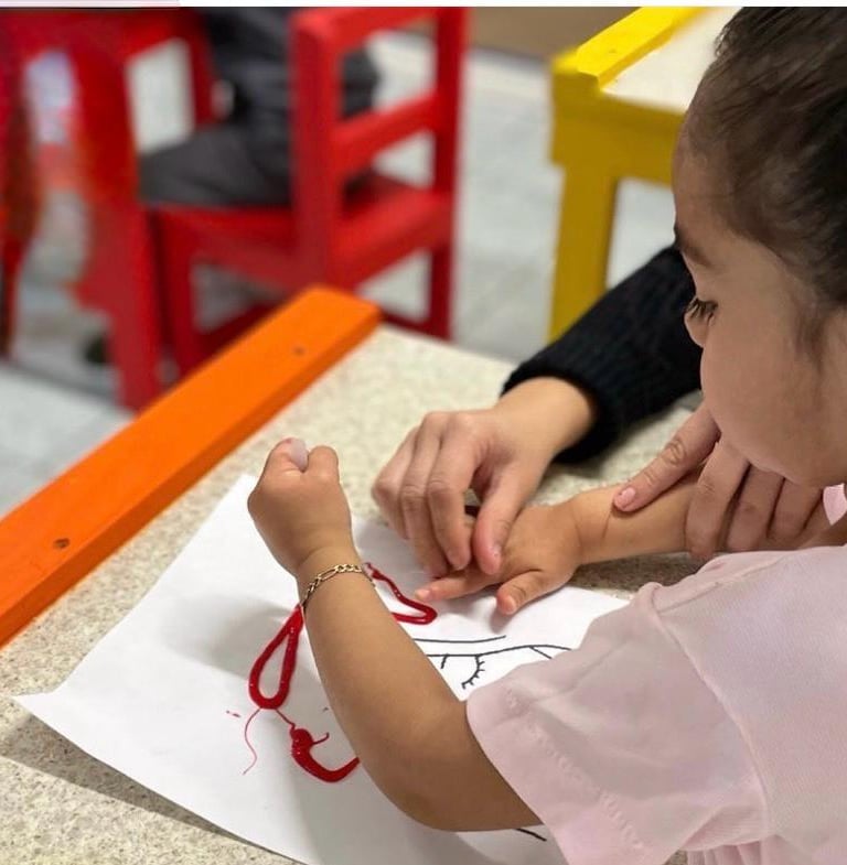 Niña en edad preescolar desarrollando la motricidad fina al pegar hilo rojo 