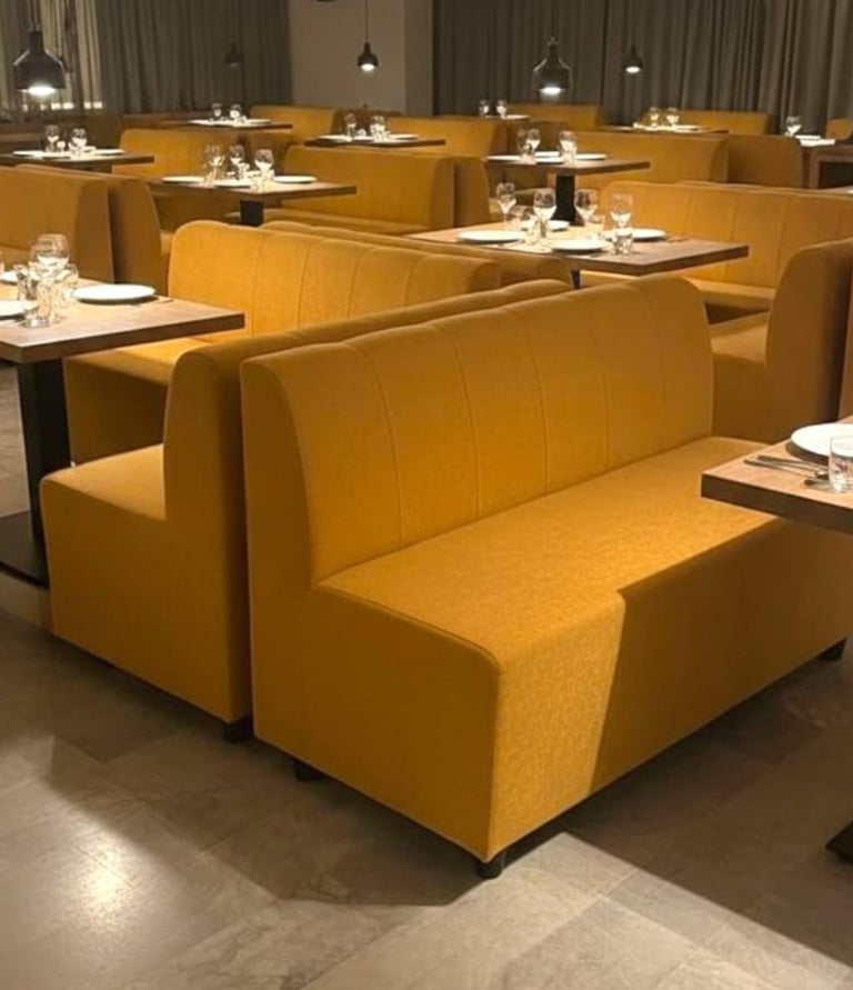 Modern restaurant interior featuring rows of mustard yellow upholstered booth seating and set dining tables.
