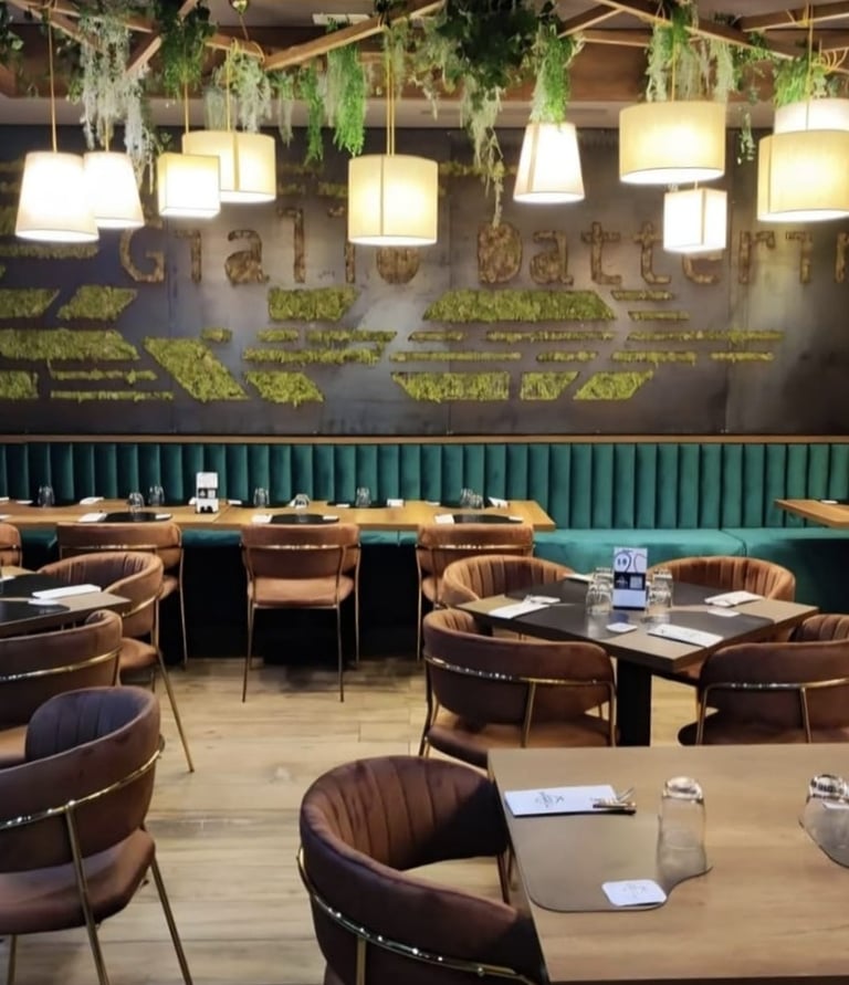 Modern restaurant interior featuring velvet chairs, green booths, and hanging plants with warm lighting.