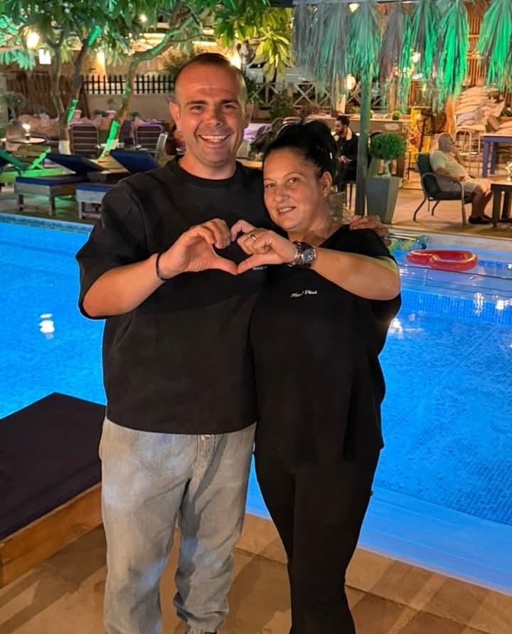 A smiling couple making a heart shape with their hands by a luxury hotel swimming pool at night.