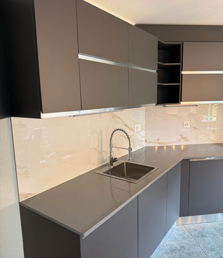 Cuisine moderne en L, meubles gris mats, plan de travail foncé et crédence effet marbre.